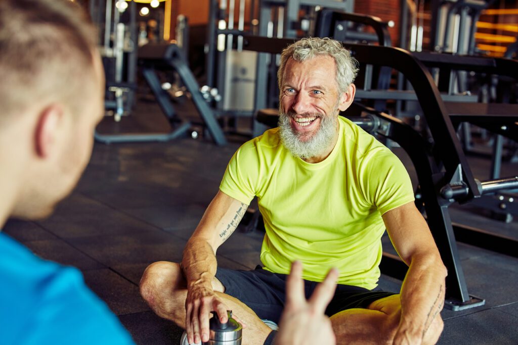 Happy middle aged man discussing something with fitness instructor or personal trainer and smiling